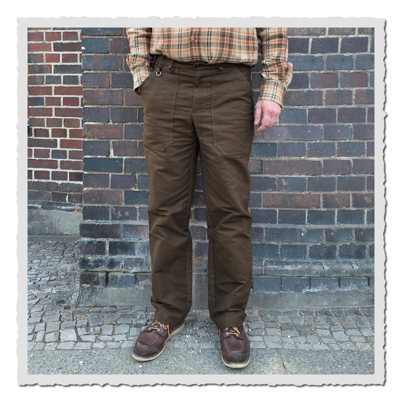 Retronia Arbeiterhose Rudolph II aus braunem Moleskin mit hoher Leibhöhe und geradem Bein im klassischen Workwear-Stil vor Ziegelwand.